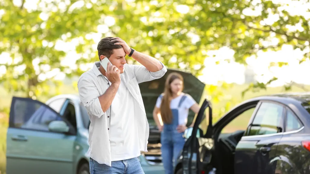 Man on the phone looking stressed after a car accident, woman in the background