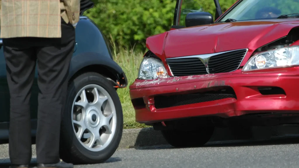 Red car with visible front-end damage after colliding with the rear side of a black vehicle on the road.
